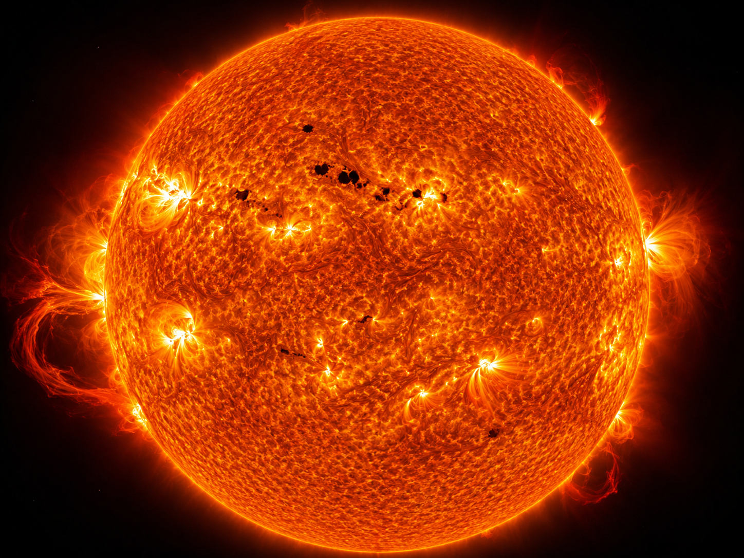 High-resolution image of the Sun showing dark sunspots, glowing prominences, and active regions across its surface.