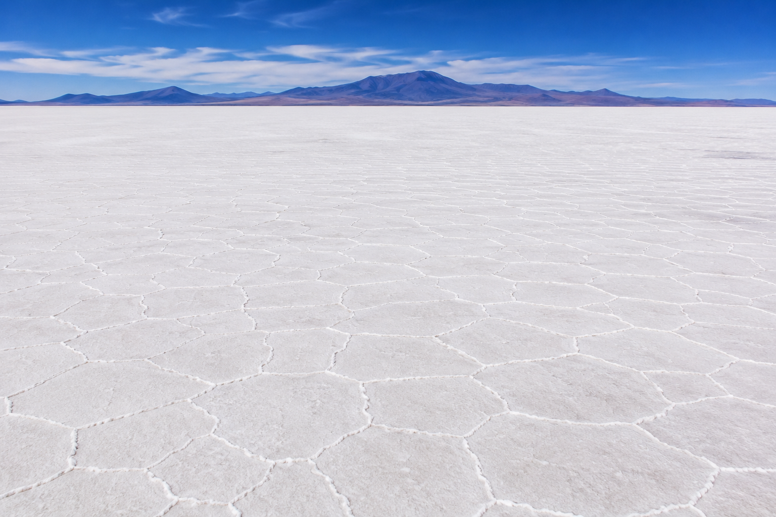 Aerial view of the vast white salt crust of Salar de Uyuni in Bolivia with the Andes mountains in the distance.