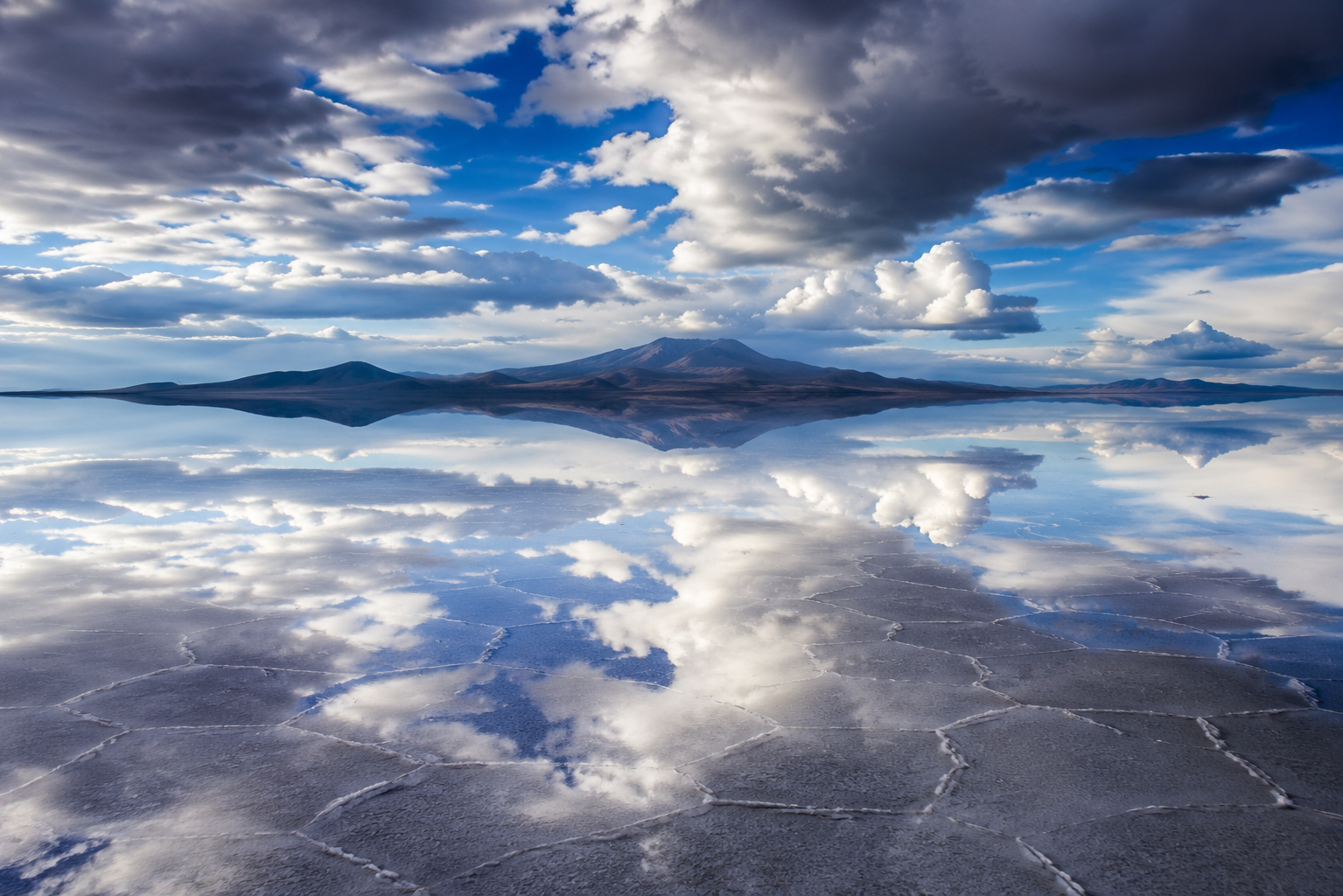 Shallow water covering Salar de Uyuni reflects the clouds and distant Andes like a giant natural mirror.