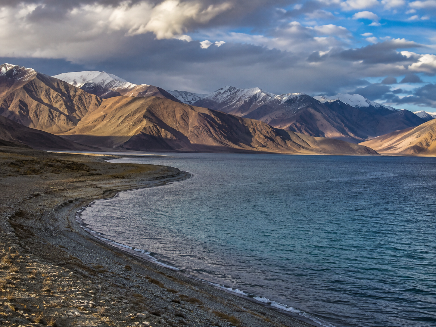 Pangong Tso stretching toward rugged Himalayan mountains under changing afternoon light.