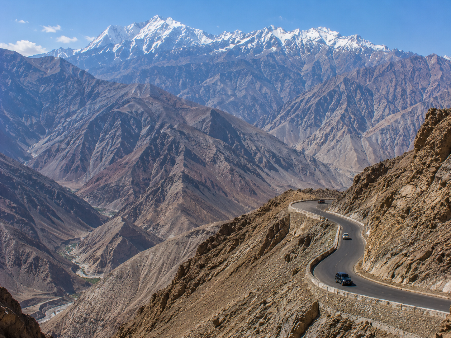 A winding mountain road crossing a vast Ladakh valley beneath rugged and snow-capped mountains.