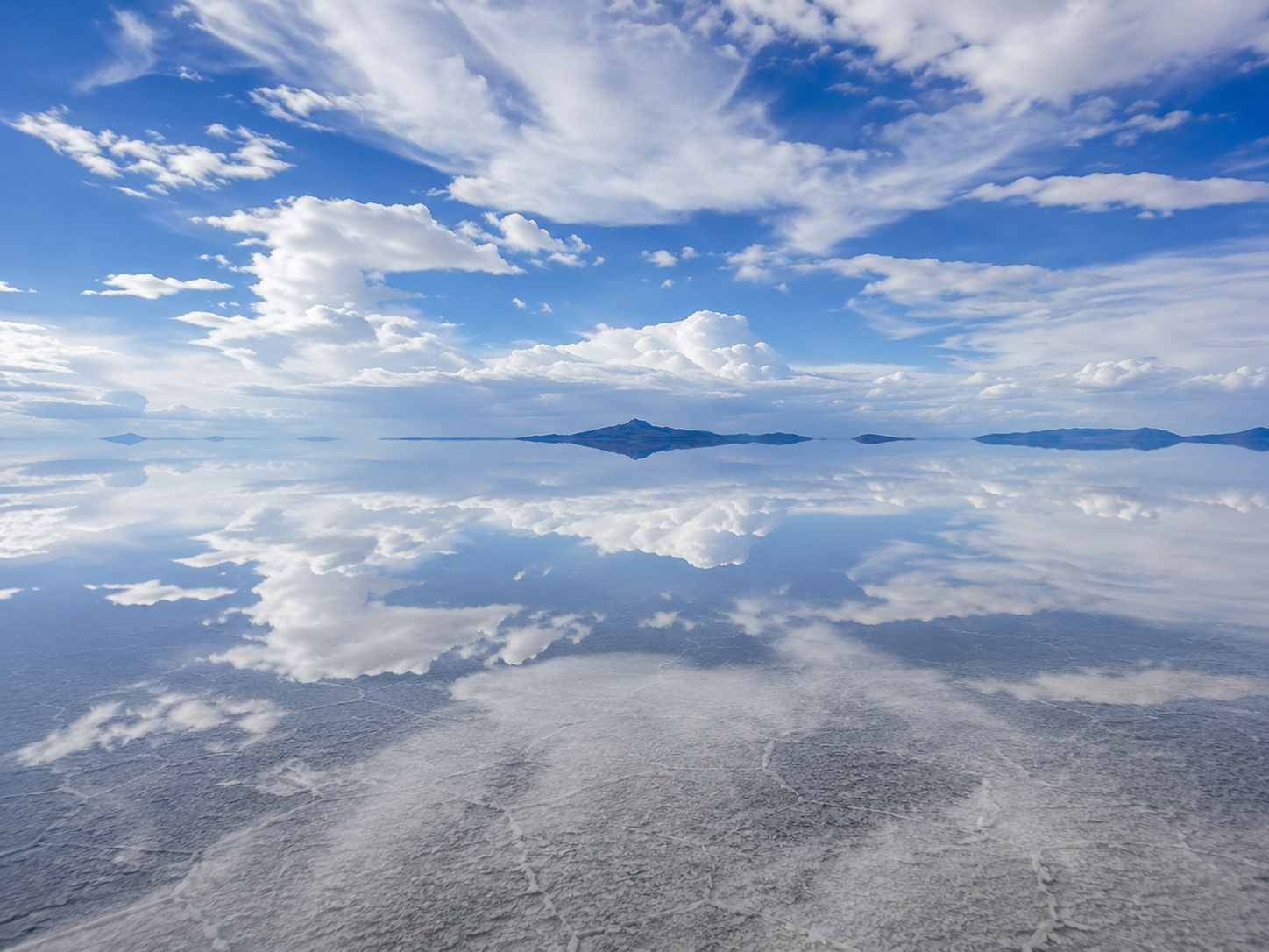 Clouds and distant mountains appear to continue beneath the surface of Salar de Uyuni.