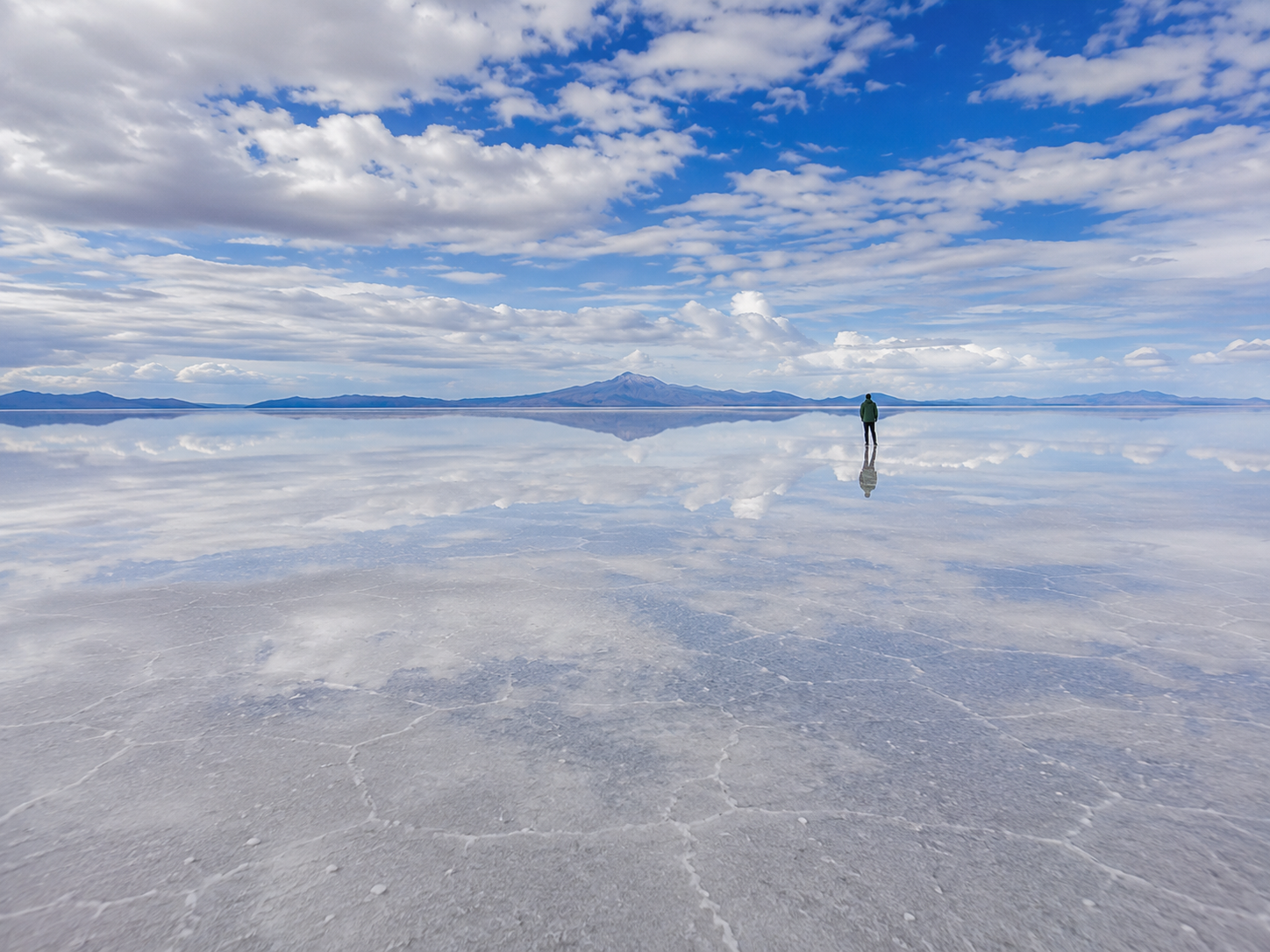 A vast shallow water layer turns Salar de Uyuni into a mirror beneath the sky and distant mountains.