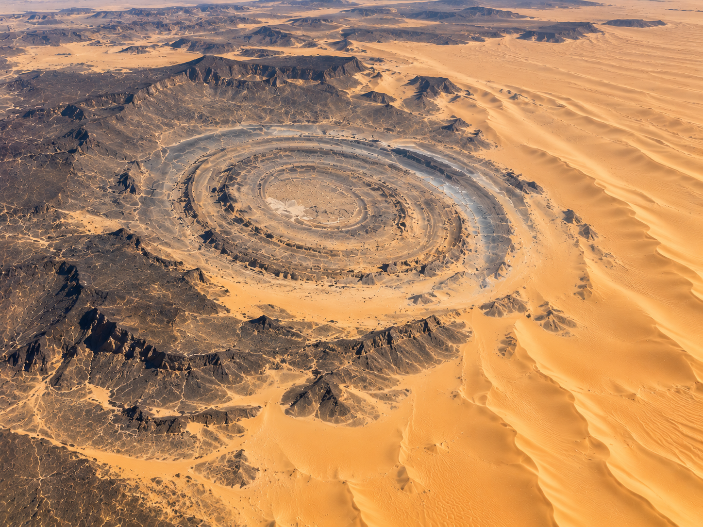 Exposed rock ridges remain visible among Sahara dunes around the Richat Structure.