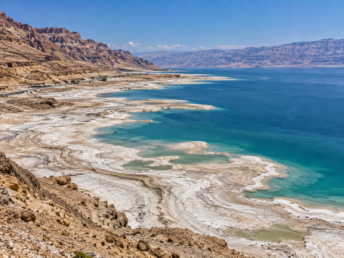 Exposed salt flats surround the retreating shoreline of the shrinking Dead Sea.