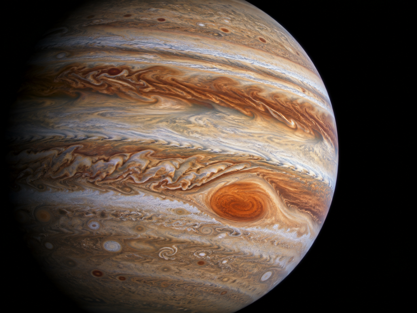 Jupiter’s Great Red Spot appears as a huge reddish storm surrounded by swirling bands of clouds across the planet’s atmosphere.